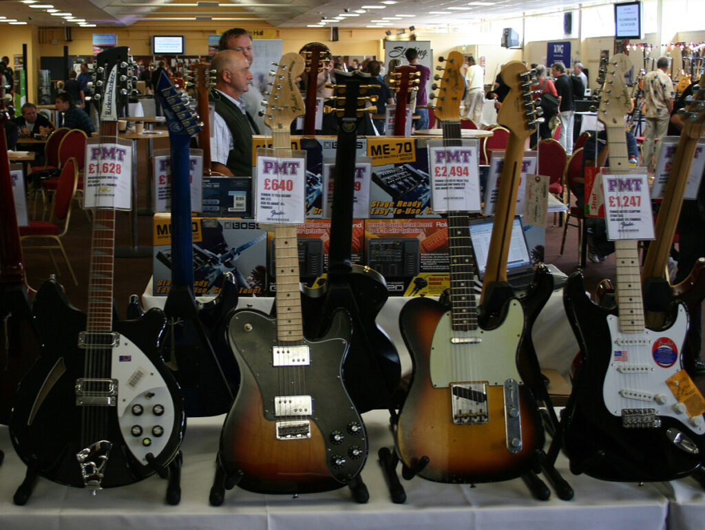 Imagem de uma variedade de guitarras expostas em um evento, com preços visíveis. Perfeita para amantes da música e músicos profissionais em busca de instrumentos de qualidade.
	
