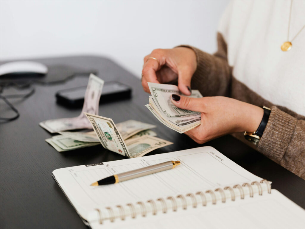 Uma pessoa contando notas de dinheiro em uma mesa, acompanhada de um caderno e uma caneta, enfatizando o gerenciamento financeiro. Investimentos no mercado da música